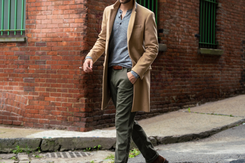 Man walking in a stylish outfit, wearing a tan coat and olive pants.