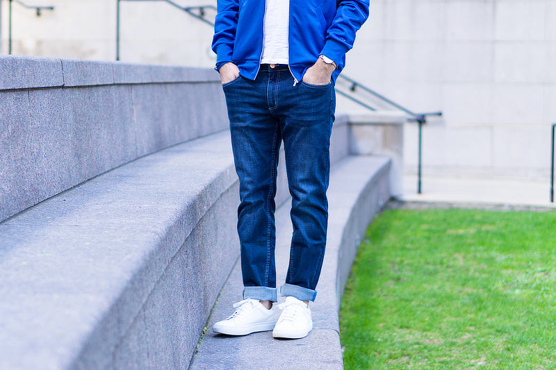 A person wearing dark jeans and white sneakers, standing on steps in a casual outfit.