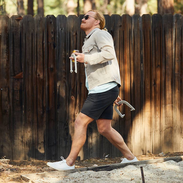 Man walking in shorts and a jacket, holding items, in a forest setting.