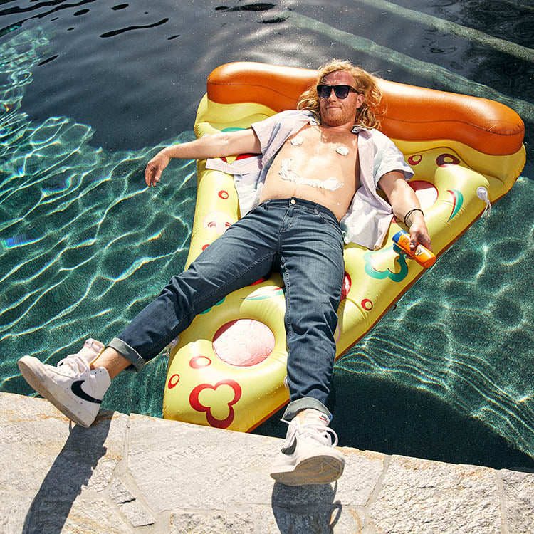 A man relaxing on a pizza-shaped float in a pool, enjoying a sunny day.