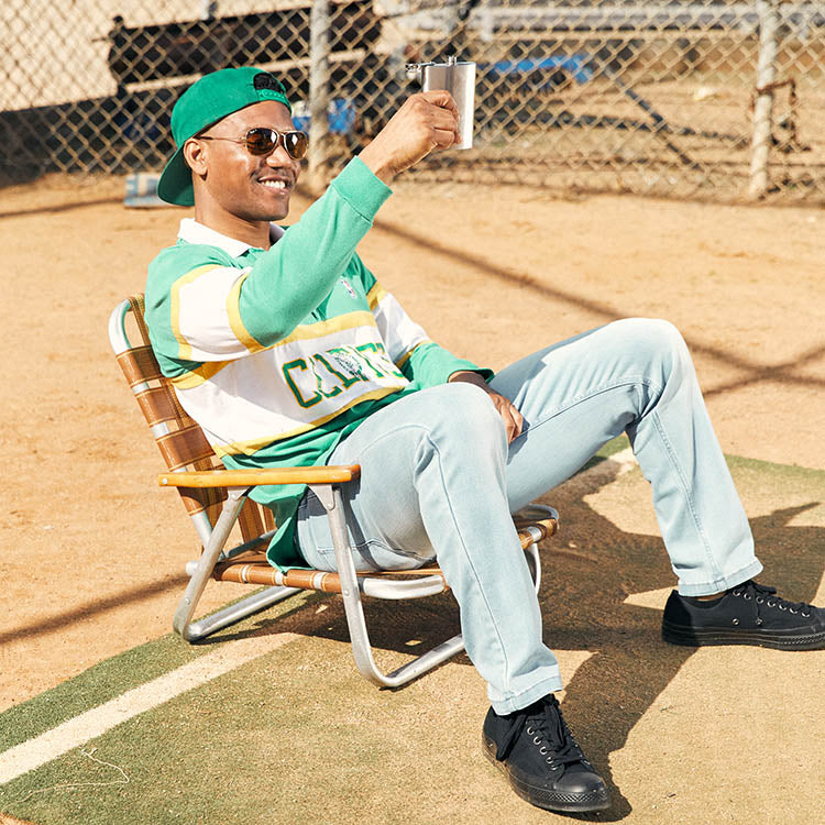 A man in a green and white striped shirt sitting in a chair, holding a drink.