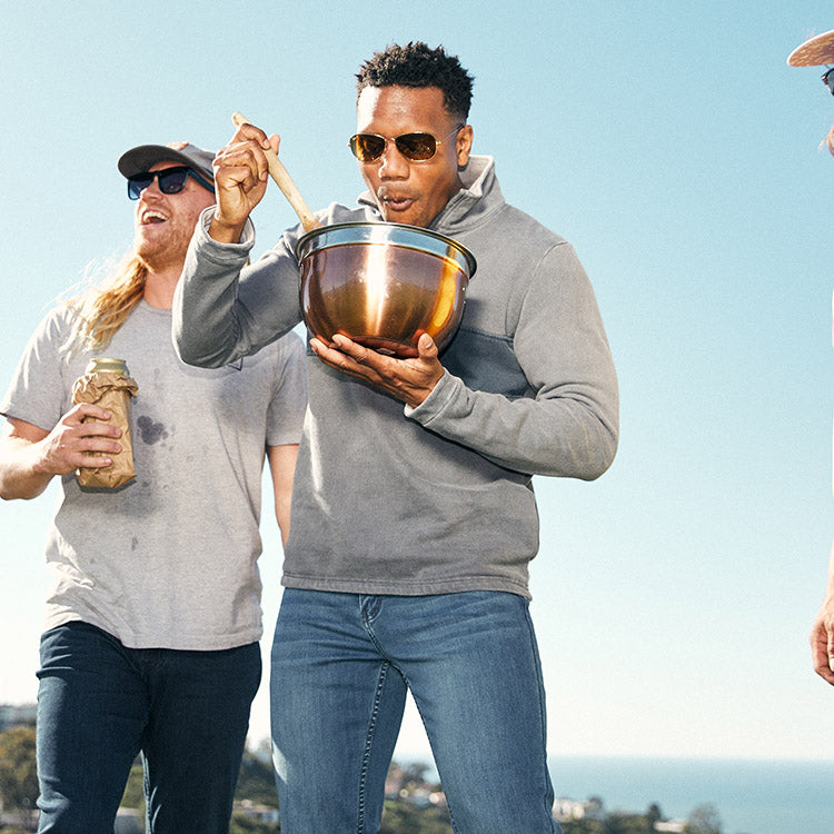 A man in sunglasses mixing in a bowl outdoors with friends in casual attire.