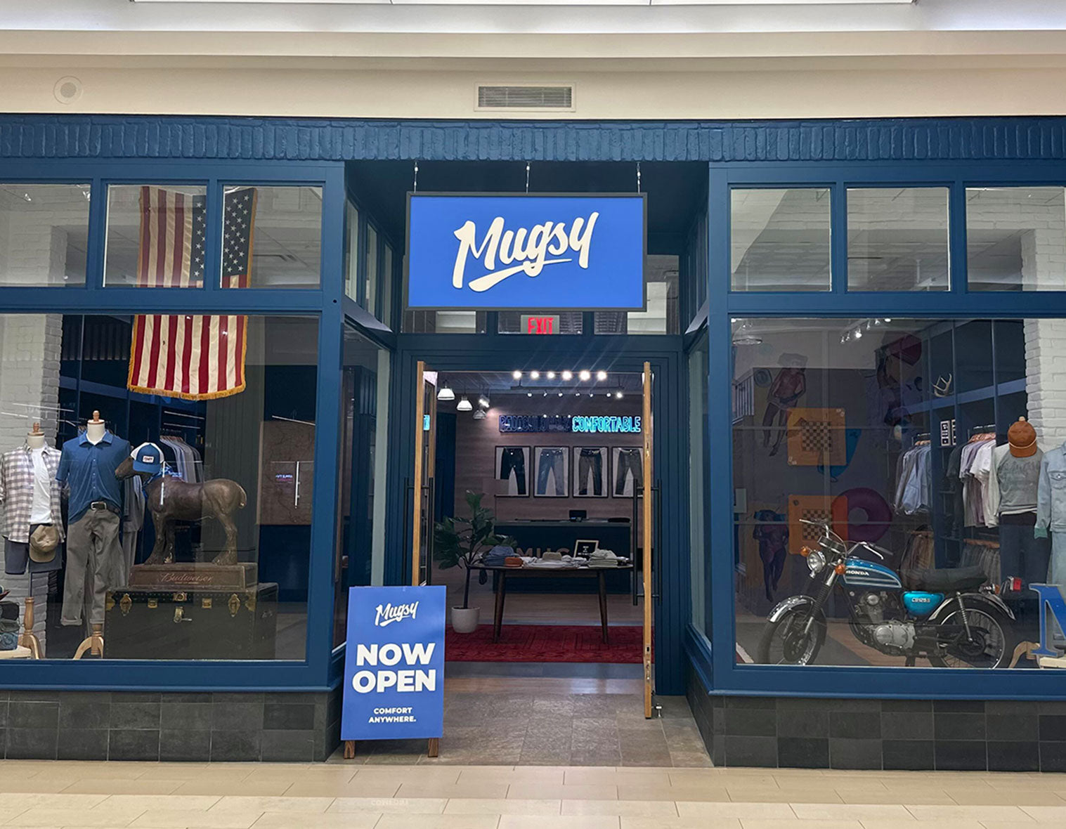 Mugsy store entrance with 'NOW OPEN' sign and American flag