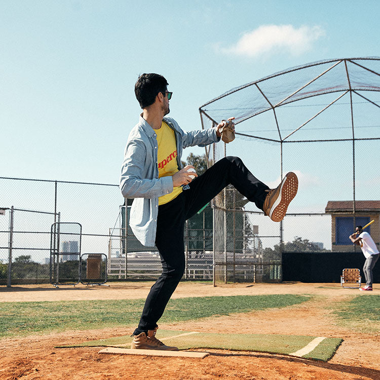 A person pitching on a baseball field, wearing casual clothing.