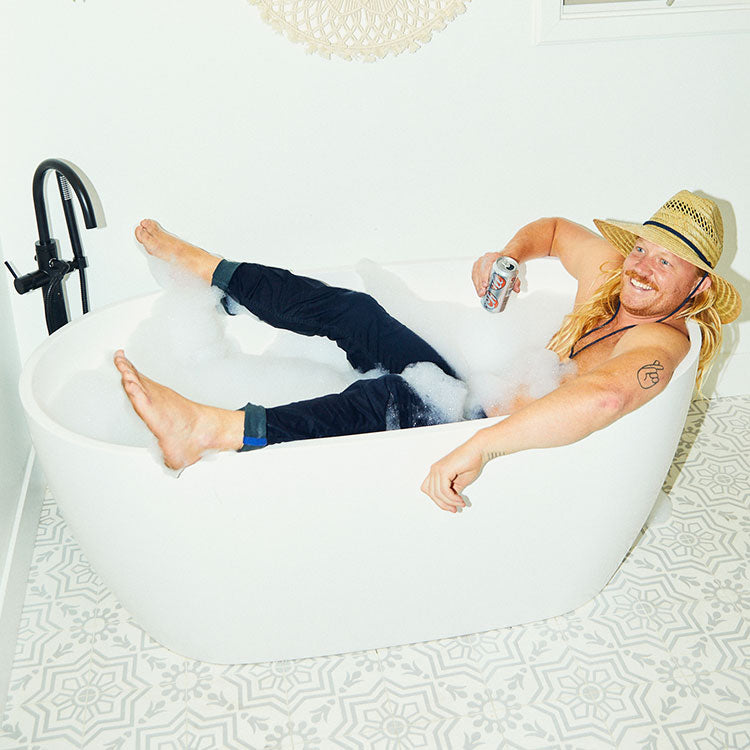 Man relaxing in a bathtub with bubbles, holding a drink.