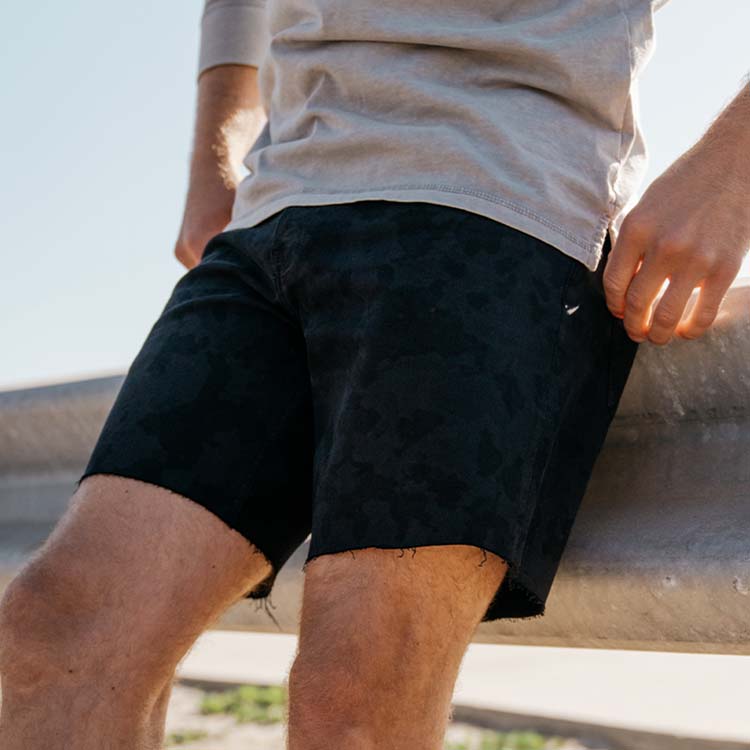 A person wearing black camo shorts, sitting on a railing.