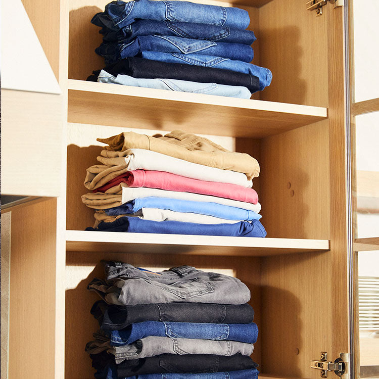 Neatly folded jeans in various colors stacked in a wooden cabinet