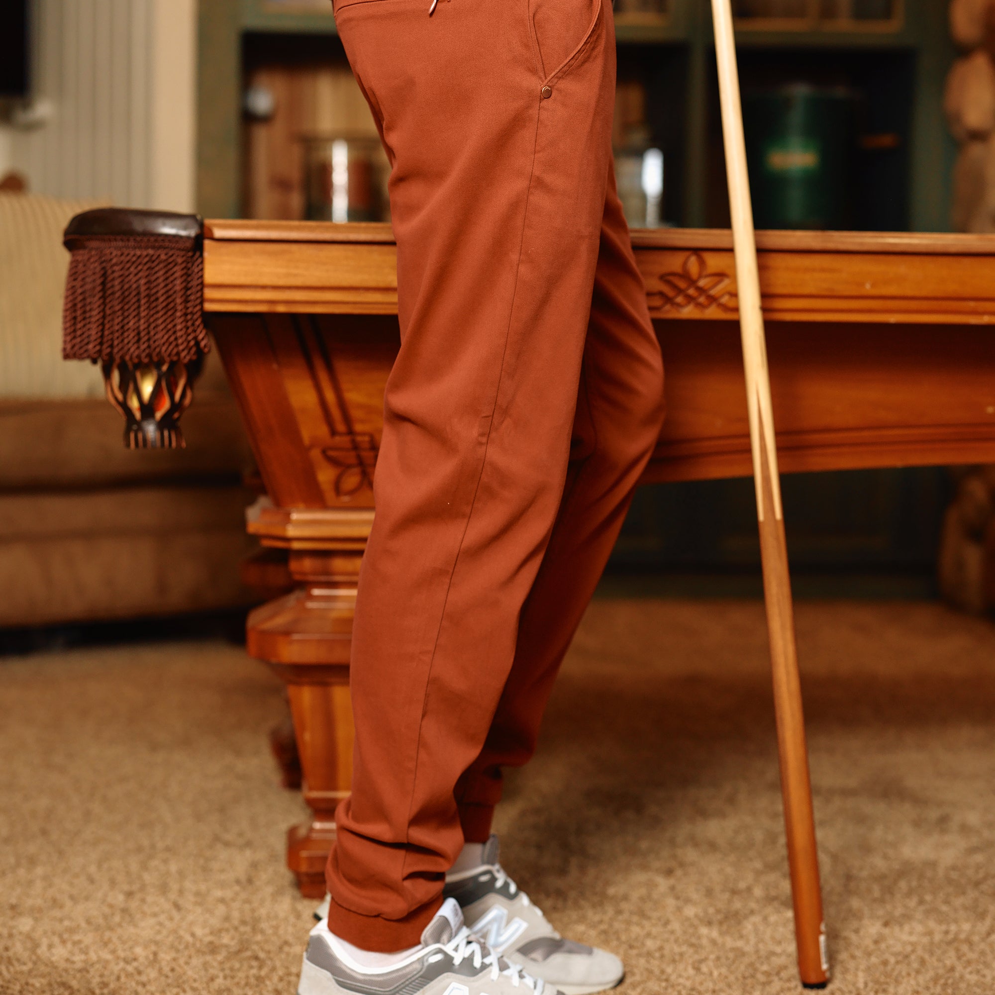 A person wearing brown joggers and gray sneakers standing next to a pool table.