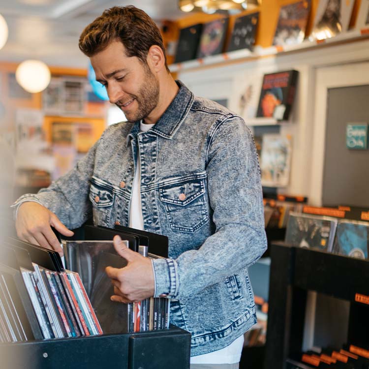 A man wearing a denim jacket browsing through vinyl records in a store.
