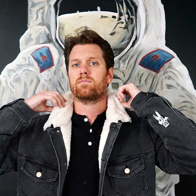 Man adjusting a sherpa-lined denim jacket in front of an astronaut mural.
