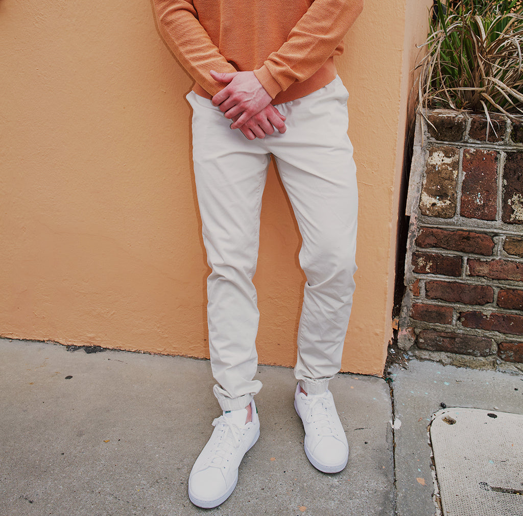 Person wearing light-colored pants and white sneakers against an orange wall.