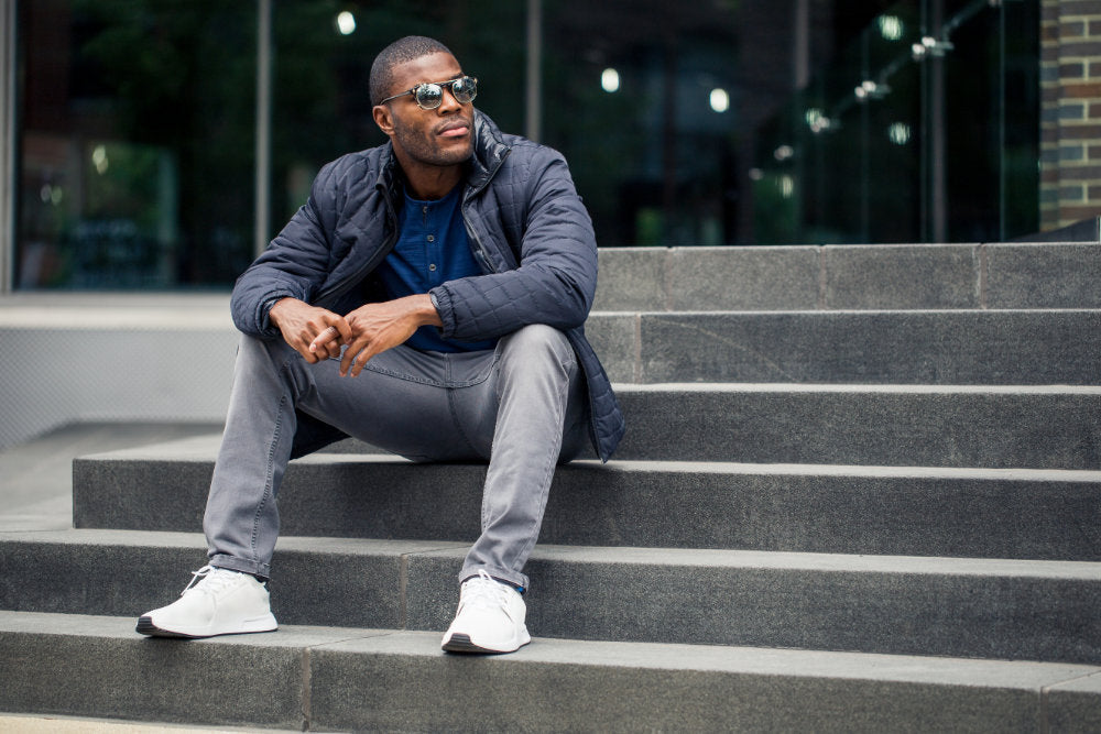 Man sitting on steps wearing gray jeans and sunglasses