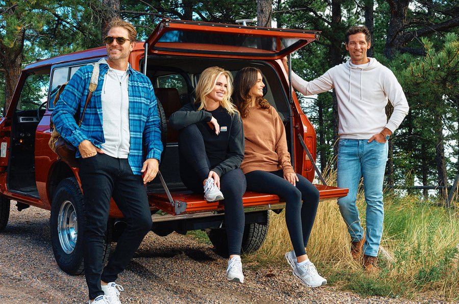 Four casually dressed adults, two men and two women, posing by the open tailgate of a red SUV in a wooded outdoor setting.