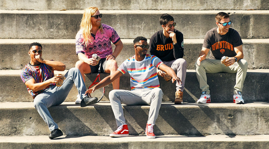 Five men sitting on sunlit concrete steps, laughing and wearing casual shirts and jeans