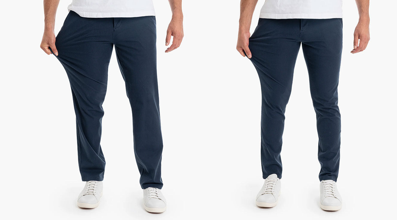 Person wearing navy chinos pulling fabric to show stretch, wearing white sneakers and a white shirt, on white background.
