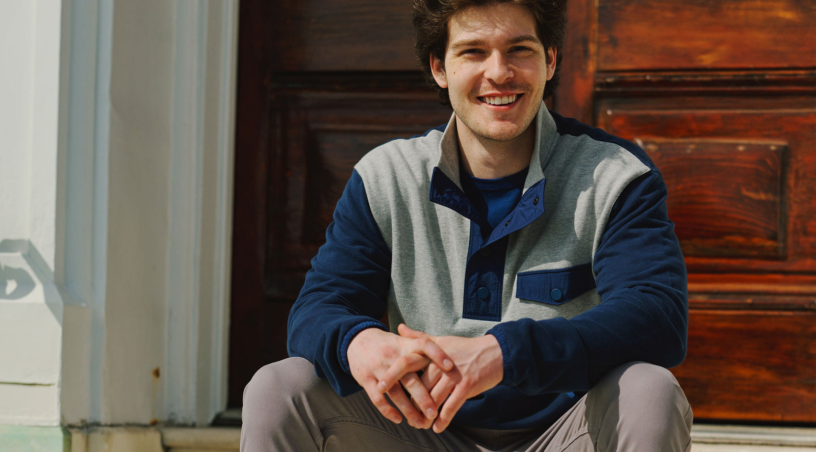 Smiling man sitting on steps wearing a navy and gray quarter zip pullover