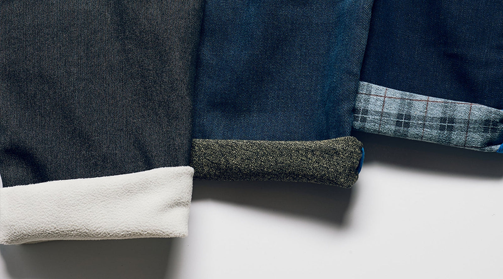 Cuffs of three winter pants showing different fabrics: dark gray with white fleece lining, blue denim with tweed cuff, and navy with gray plaid cuff.