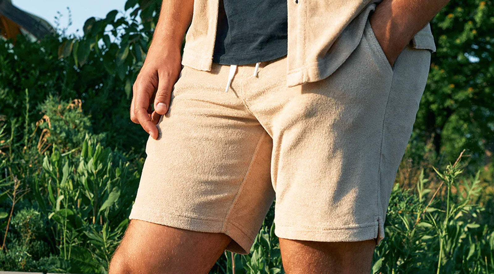 Man wearing beige terry knit shorts outdoors with greenery in the background