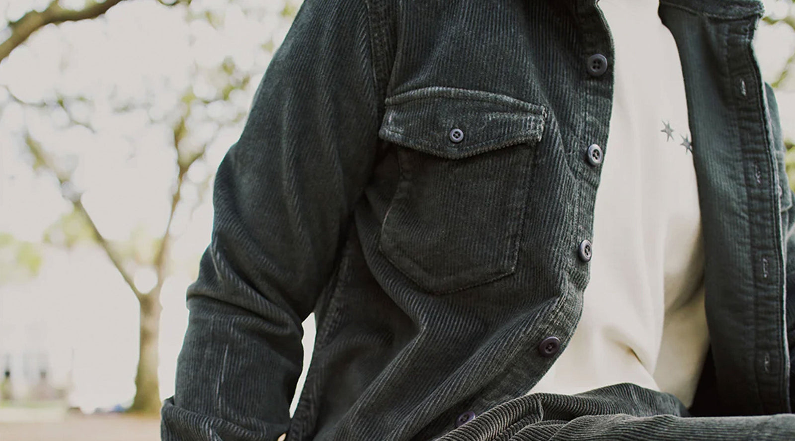 Person wearing a dark green corduroy jacket and matching pants sitting outdoors