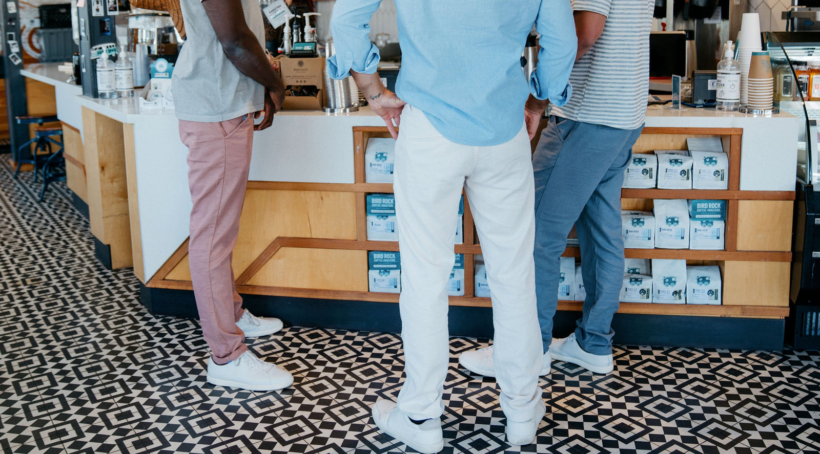 Three men standing at a coffee shop counter with shelves of Bird Rock Coffee Roasters bags visible below the counter.