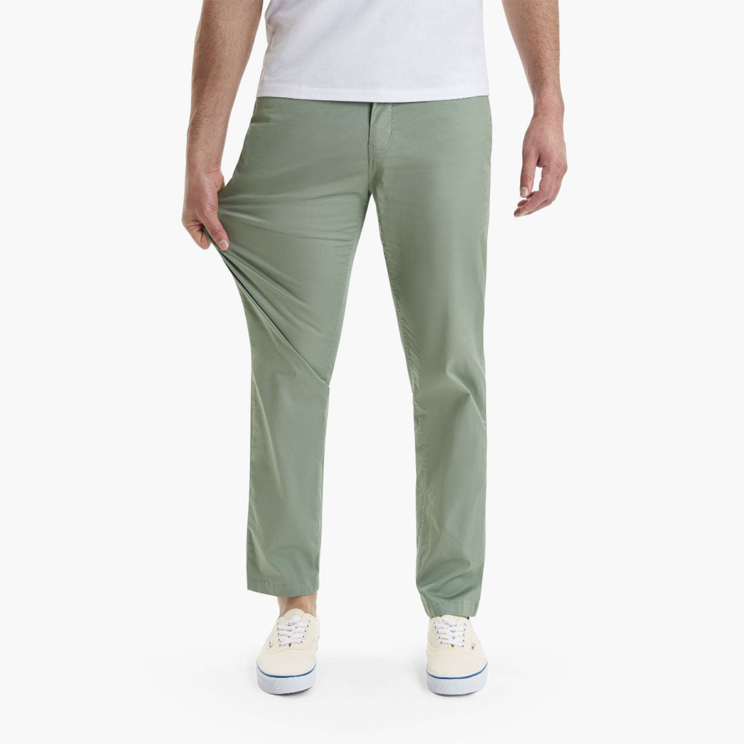 A person demonstrating the fit of green pants by holding the waistband.
