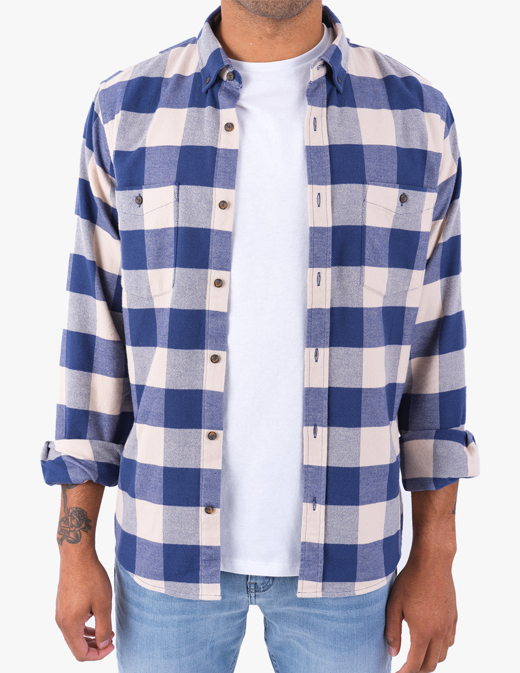 Adult male wearing blue-and-cream check flannel shirt unbuttoned over white T-shirt, rolled sleeves, left forearm tattoo.