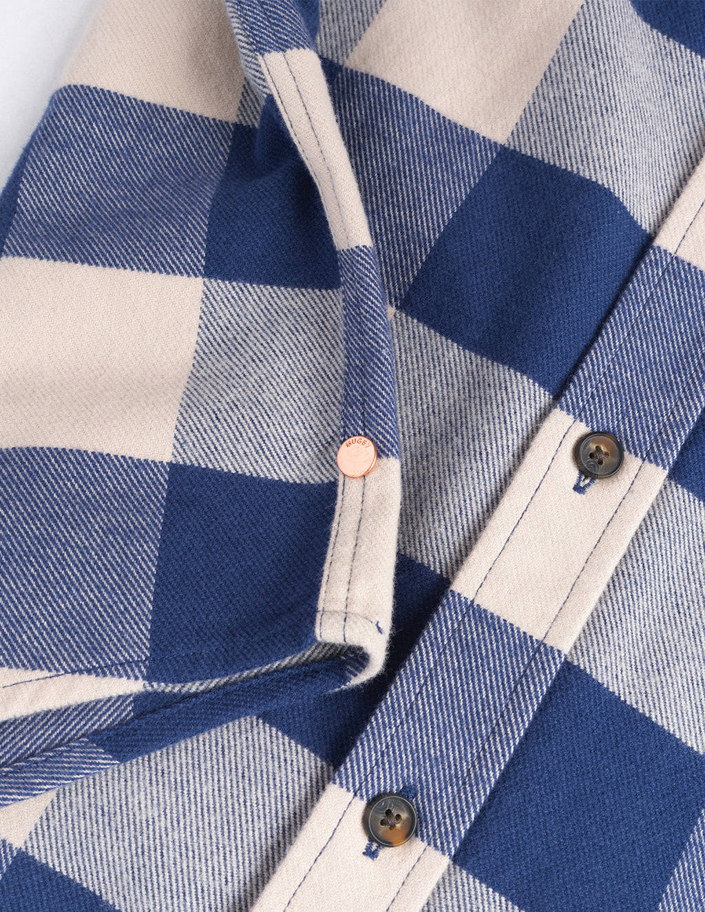 Close-up of blue-and-cream buffalo-plaid flannel shirt showing stitched button placket, horn buttons, and a small copper rivet.
