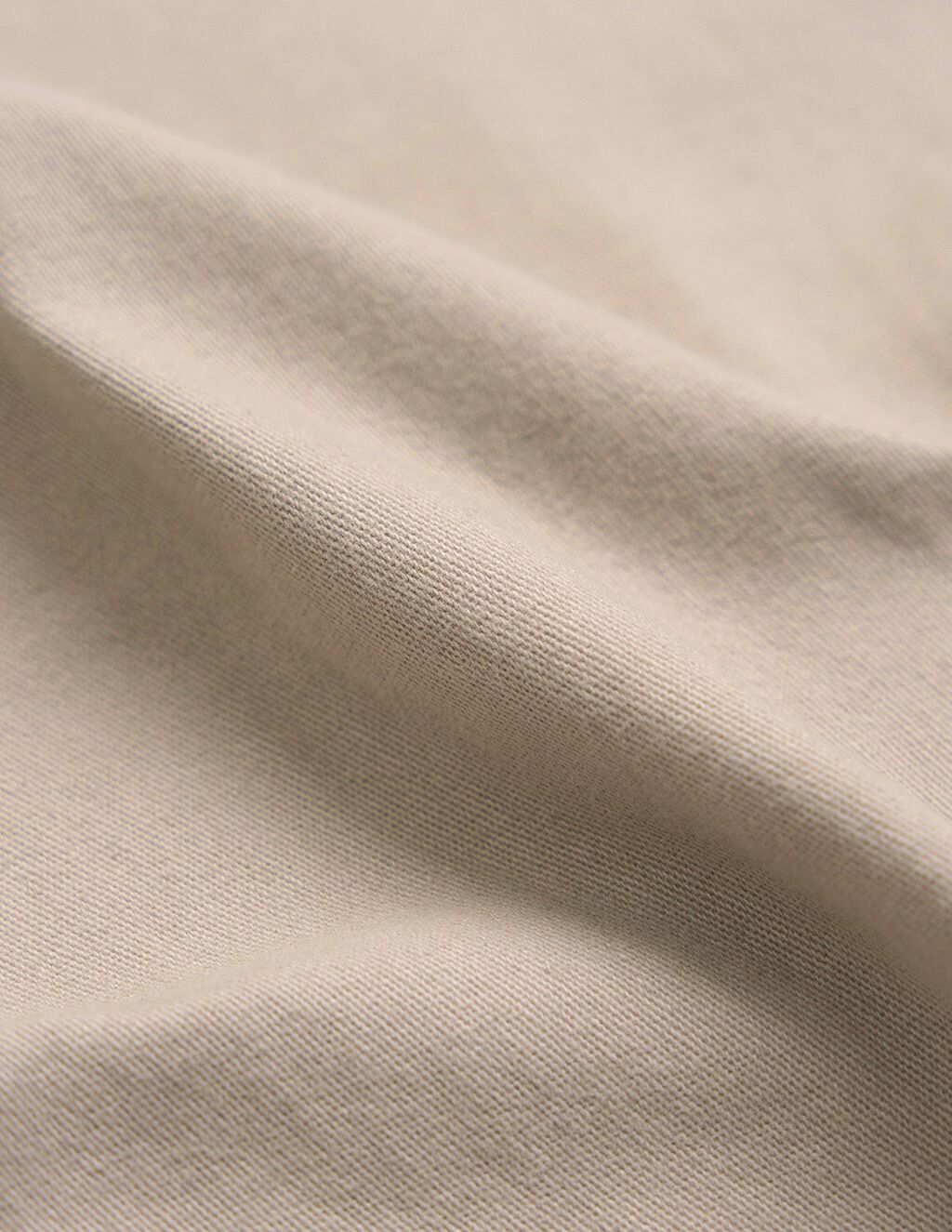 Beige knit fabric close-up showing soft folds and the woven texture.