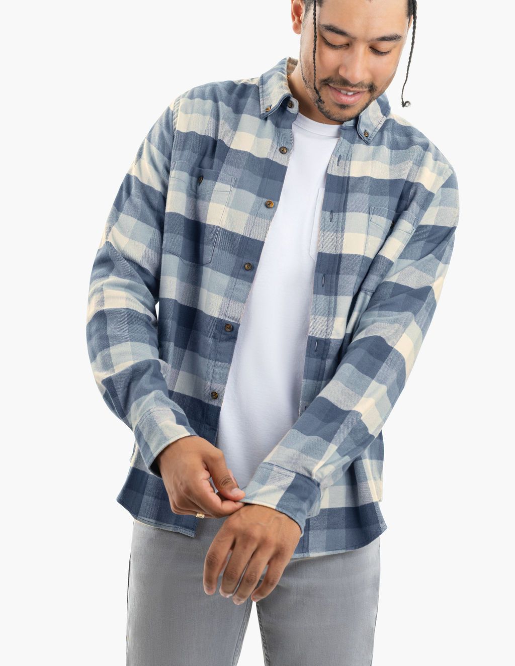 Smiling man adjusting cuff of blue and white plaid button-up shirt over a white t-shirt