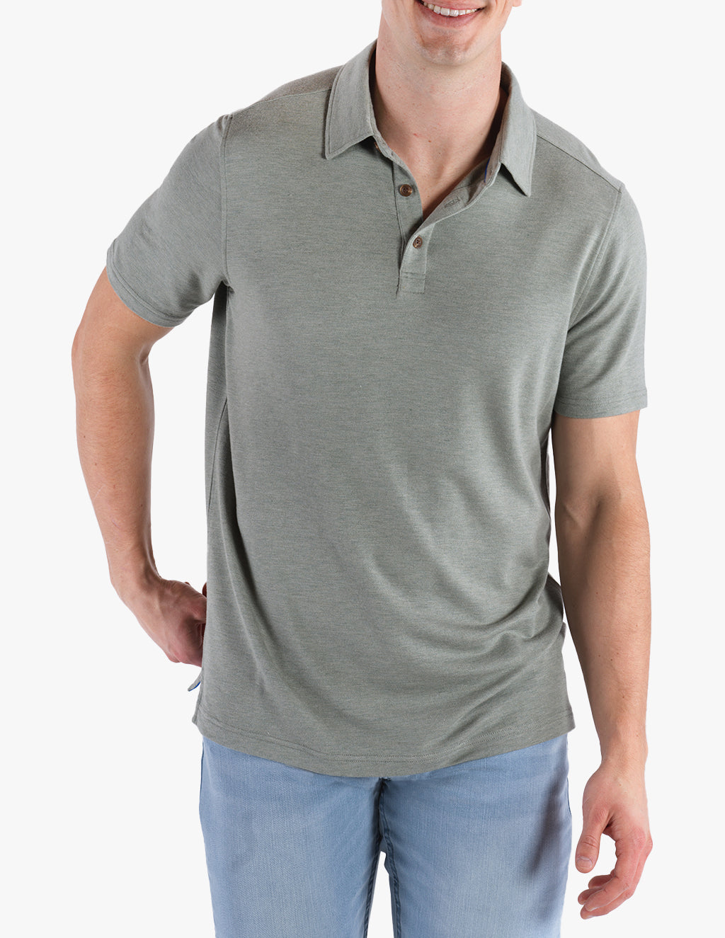 Man wearing a light green polo shirt and light blue pants, smiling with one hand behind his back.