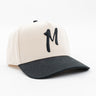 Cream baseball cap with black brim and embroidered M on front, angled on white background