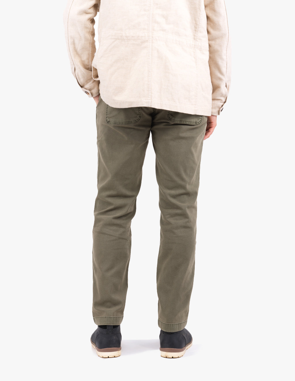 Rear view of person wearing olive-green pants and beige jacket, hands in back pockets, black shoes with light soles