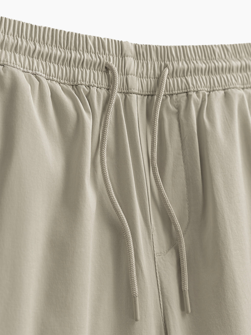 Close-up of khaki twill joggers waistband showing elastic waistband and braided drawcord on white background