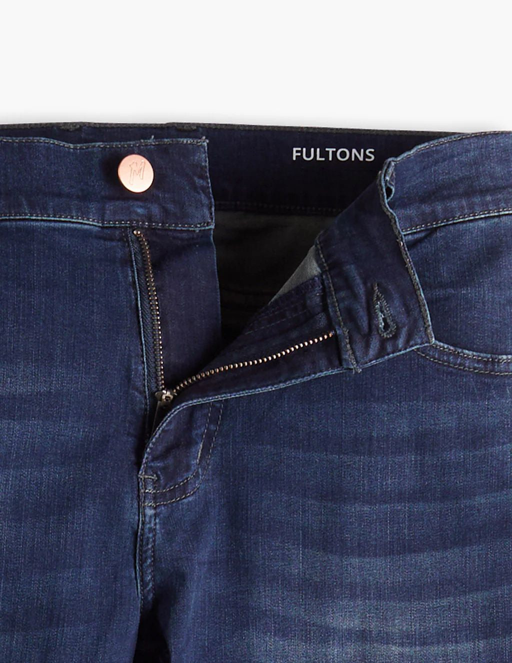 Close-up of dark blue jeans with zipper partially open, copper button, and inside label reading 'FULTONS'
