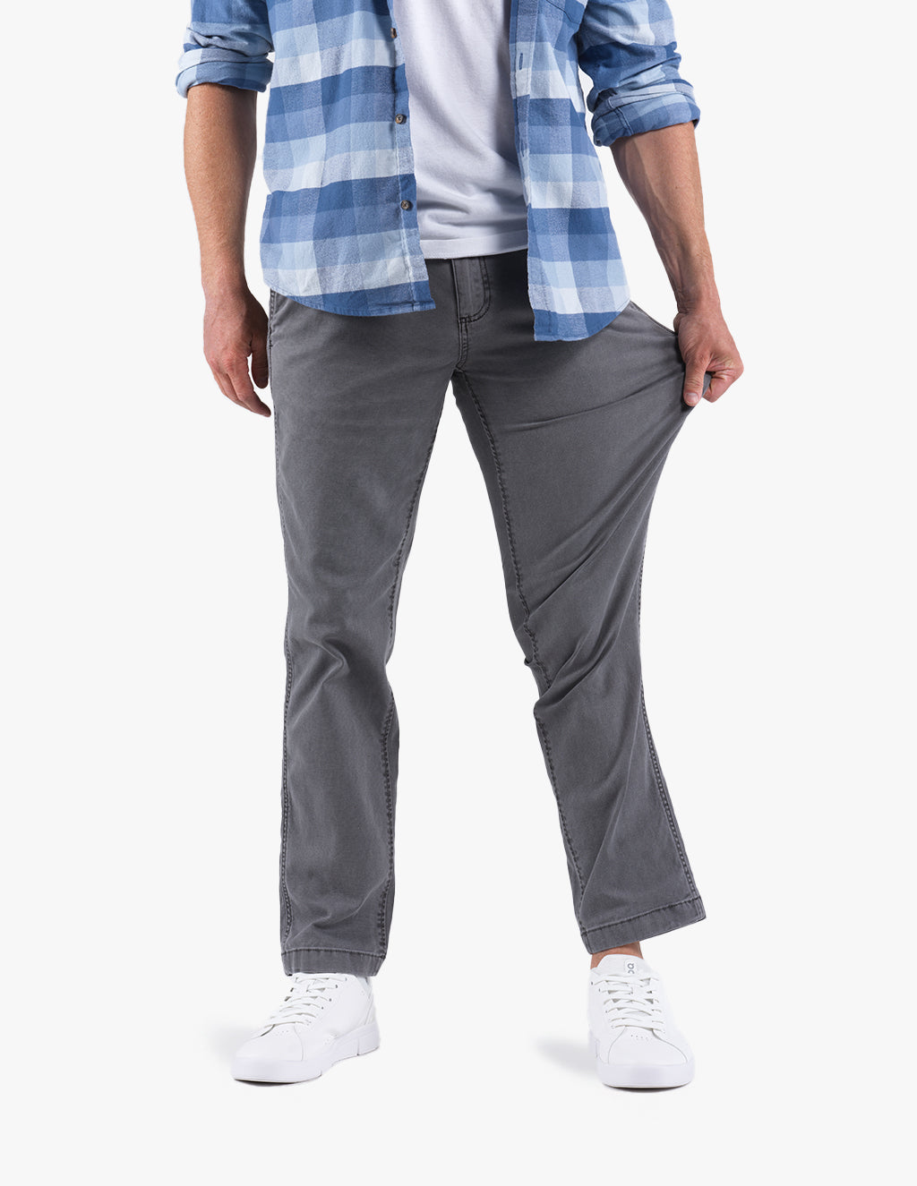 Model wearing gray stretch jeans, pulling thigh to show fabric stretch; white sneakers and blue plaid shirt visible.