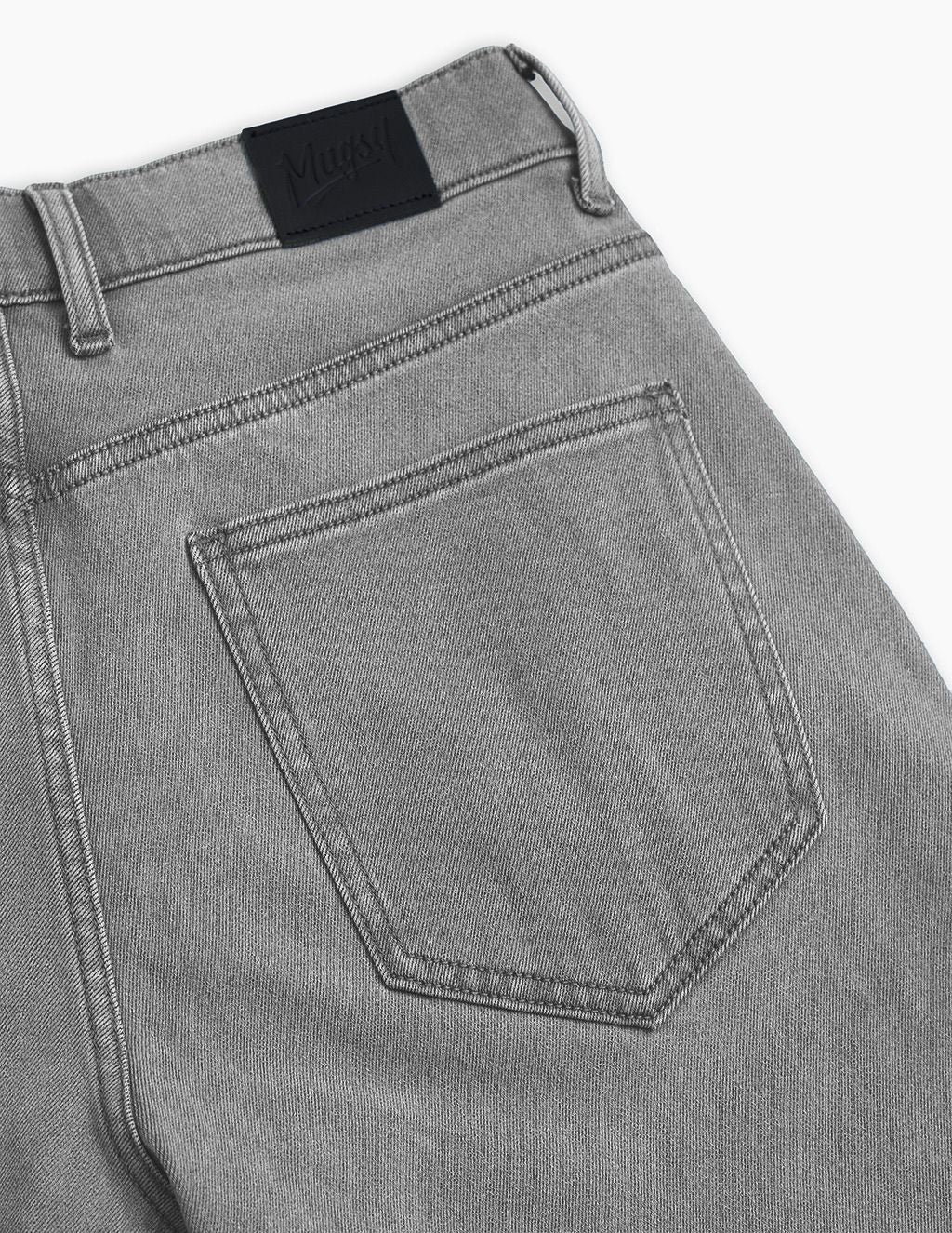 Back of grey denim jeans showing back pocket, topstitching and leather brand patch reading 'Mavi'.