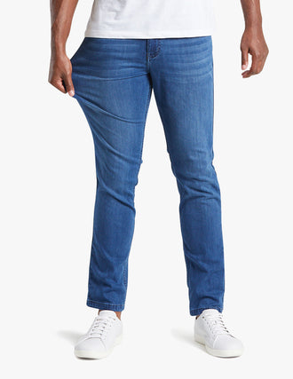 Man wearing Lake Shores blue jeans stretching the fabric to show its stretchiness, wearing white sneakers