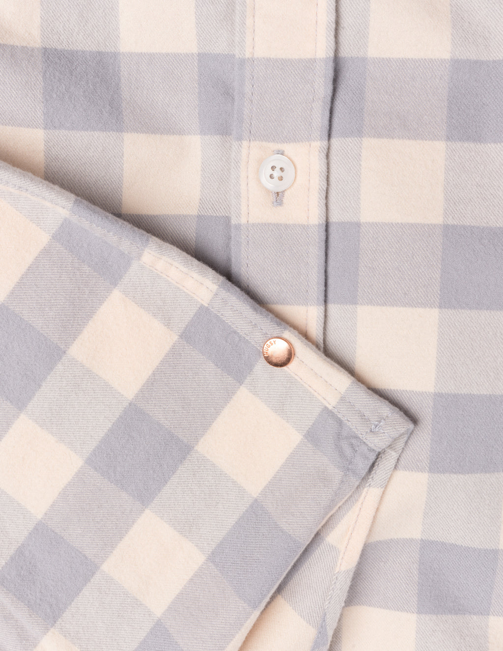 Close-up of a beige and gray checkered shirt showing a white button and a copper rivet engraved with 'HUGSY'.