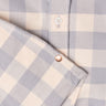Close-up of a beige and gray checkered shirt showing a white button and a copper rivet engraved with 'HUGSY'.