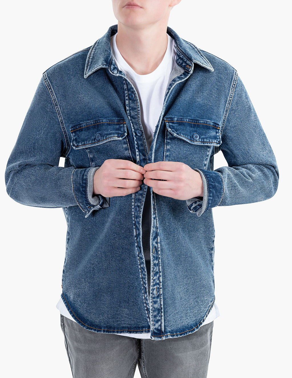 Model wearing a blue denim overshirt, buttoning it up.