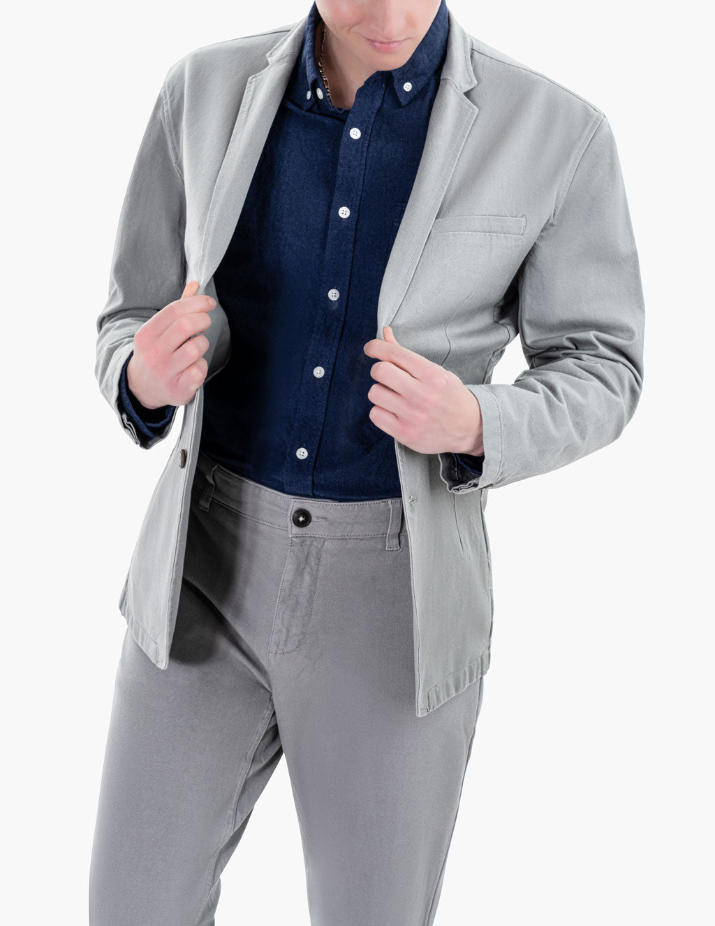 A person wearing a gray blazer over a navy shirt and gray pants, adjusting the blazer.
