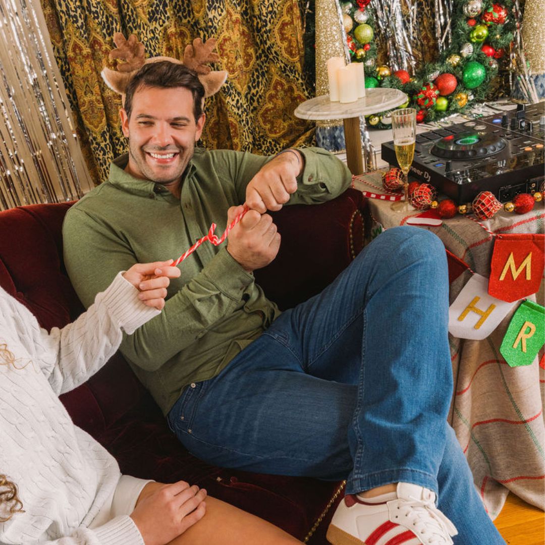 Smiling man in reindeer antlers on couch pulling a candy cane; holiday decor, Pioneer DJ controller and banner reading M H R.