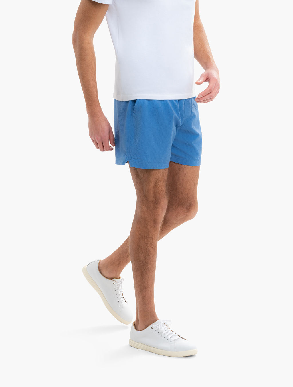 Three-quarter view of Pacifics swim shorts in blue on a model, showing textured fabric, short inseam and side notch against a white background
