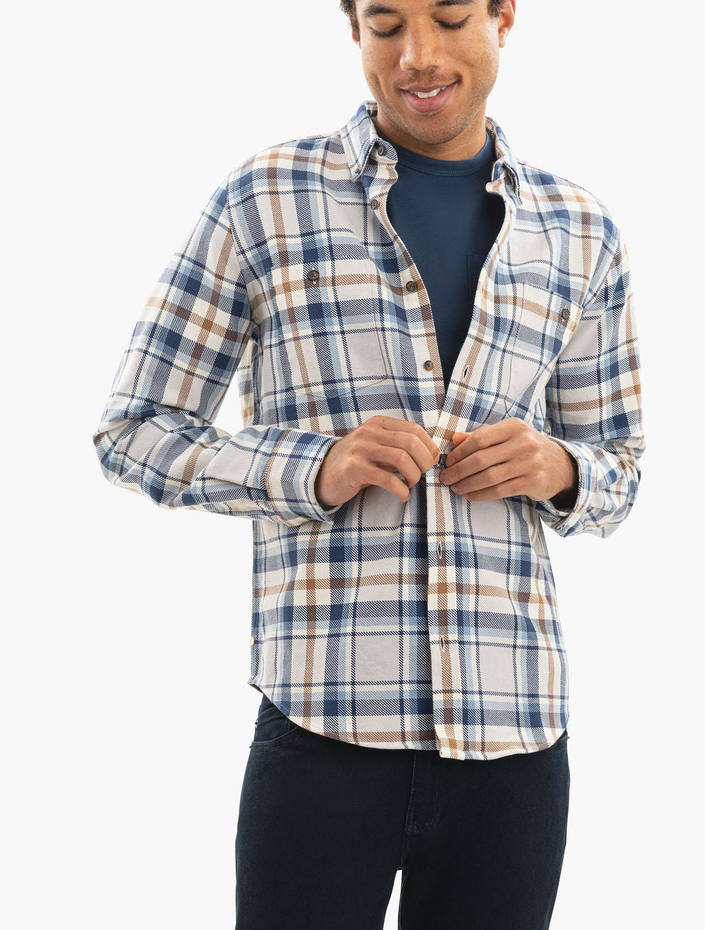 Man buttoning a blue, brown, and white plaid shirt over a navy T-shirt.