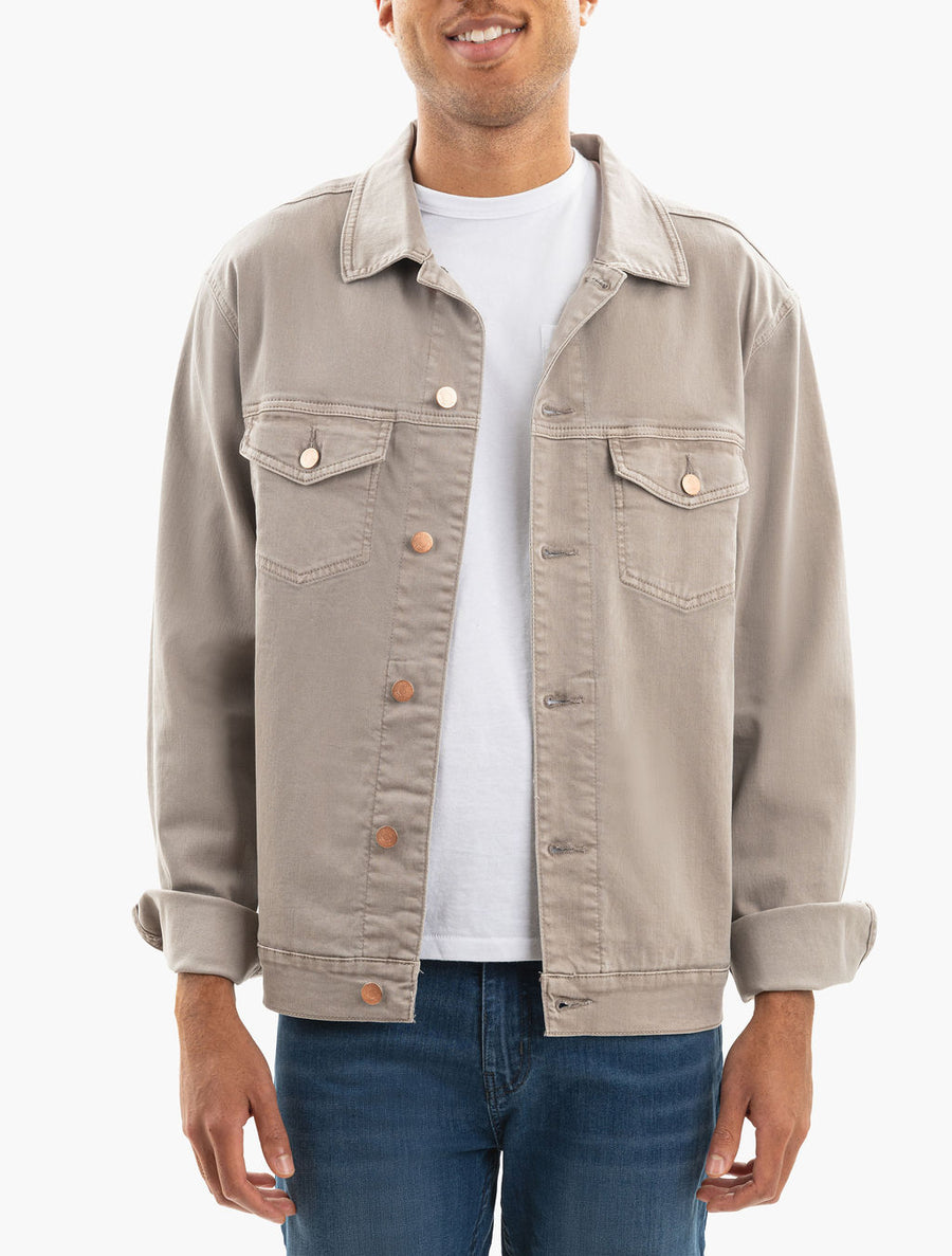 Smiling man in a light beige denim jacket over a white t-shirt and blue jeans, sleeves rolled.
