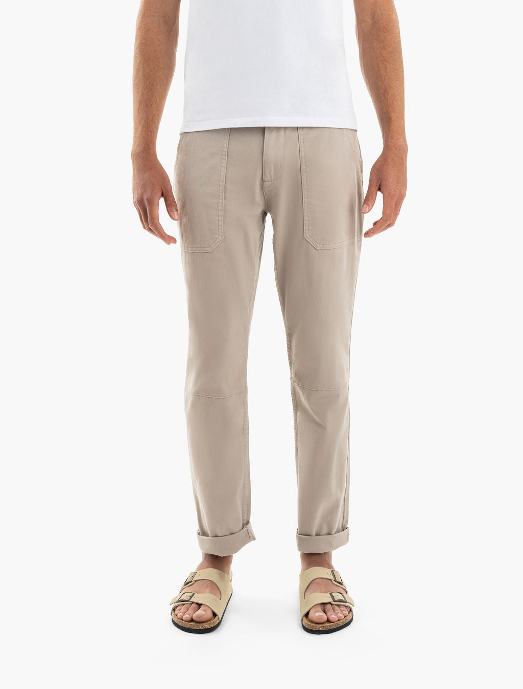 Men's beige tapered pants with front patch pockets and rolled cuffs, shown on model wearing sandals.