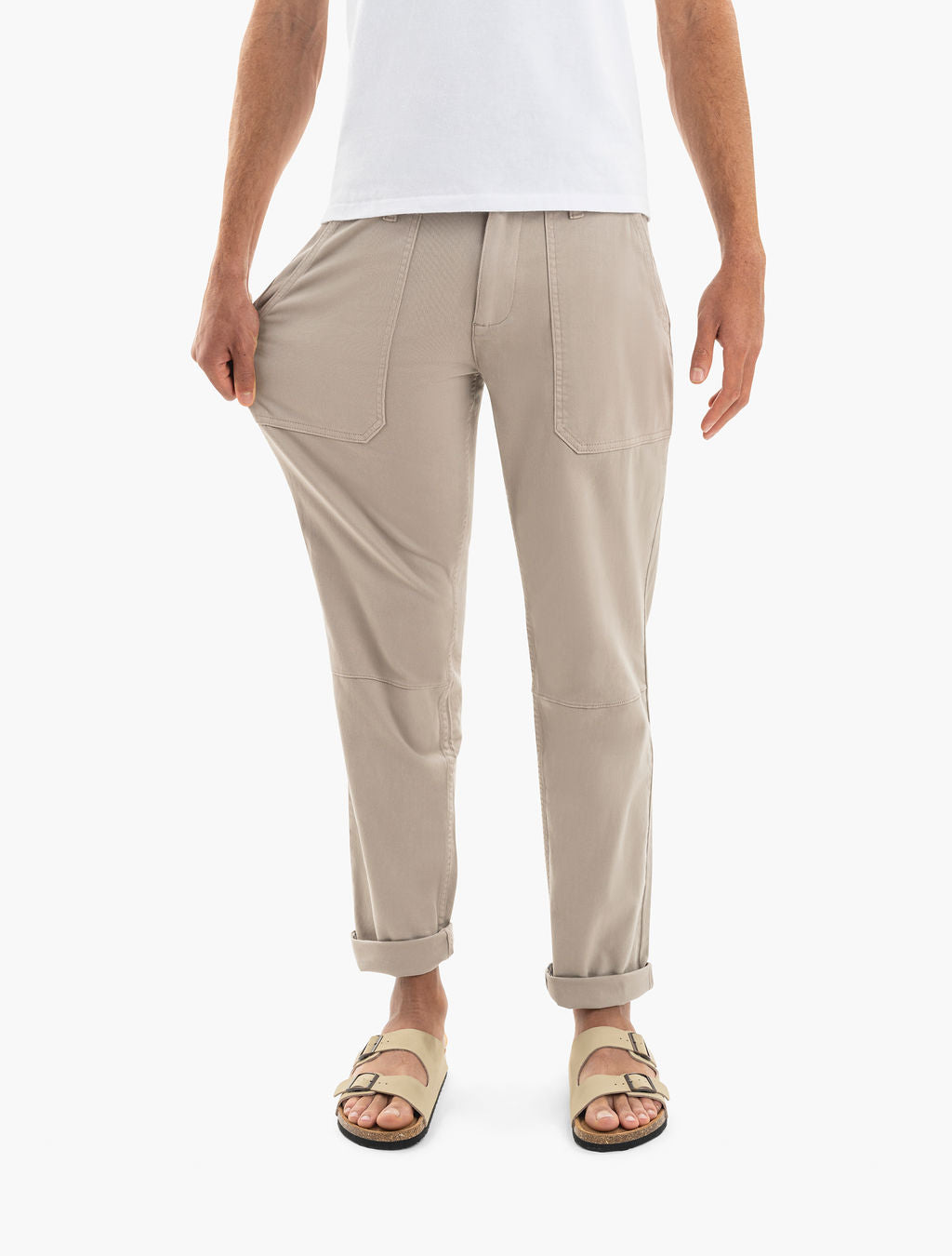 Beige pants with front patch pockets and rolled cuffs; model pulls thigh to show fabric stretch, wearing two-strap sandals.