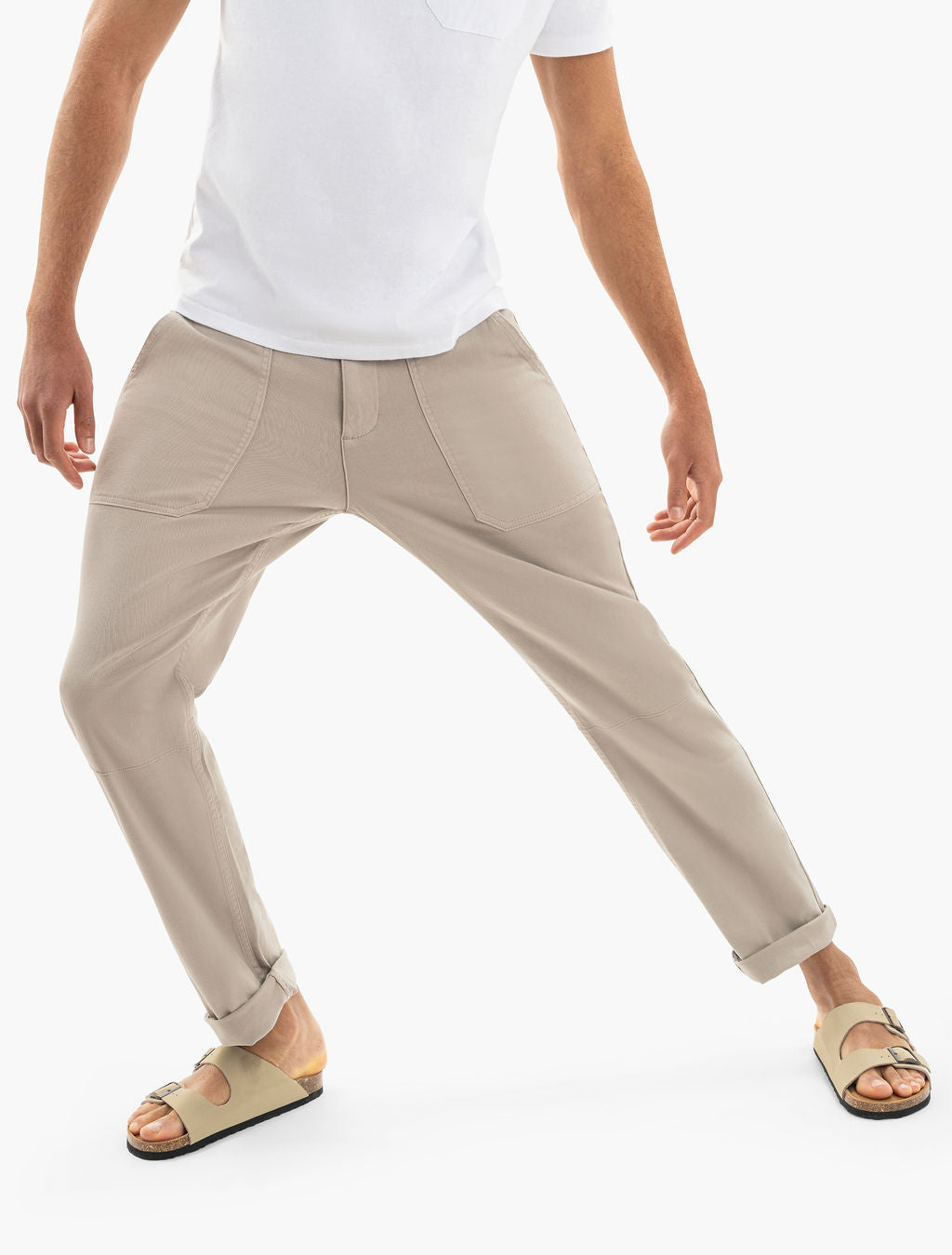 Beige tapered pants on model with rolled cuffs, white tee and beige slide sandals, legs in wide stance