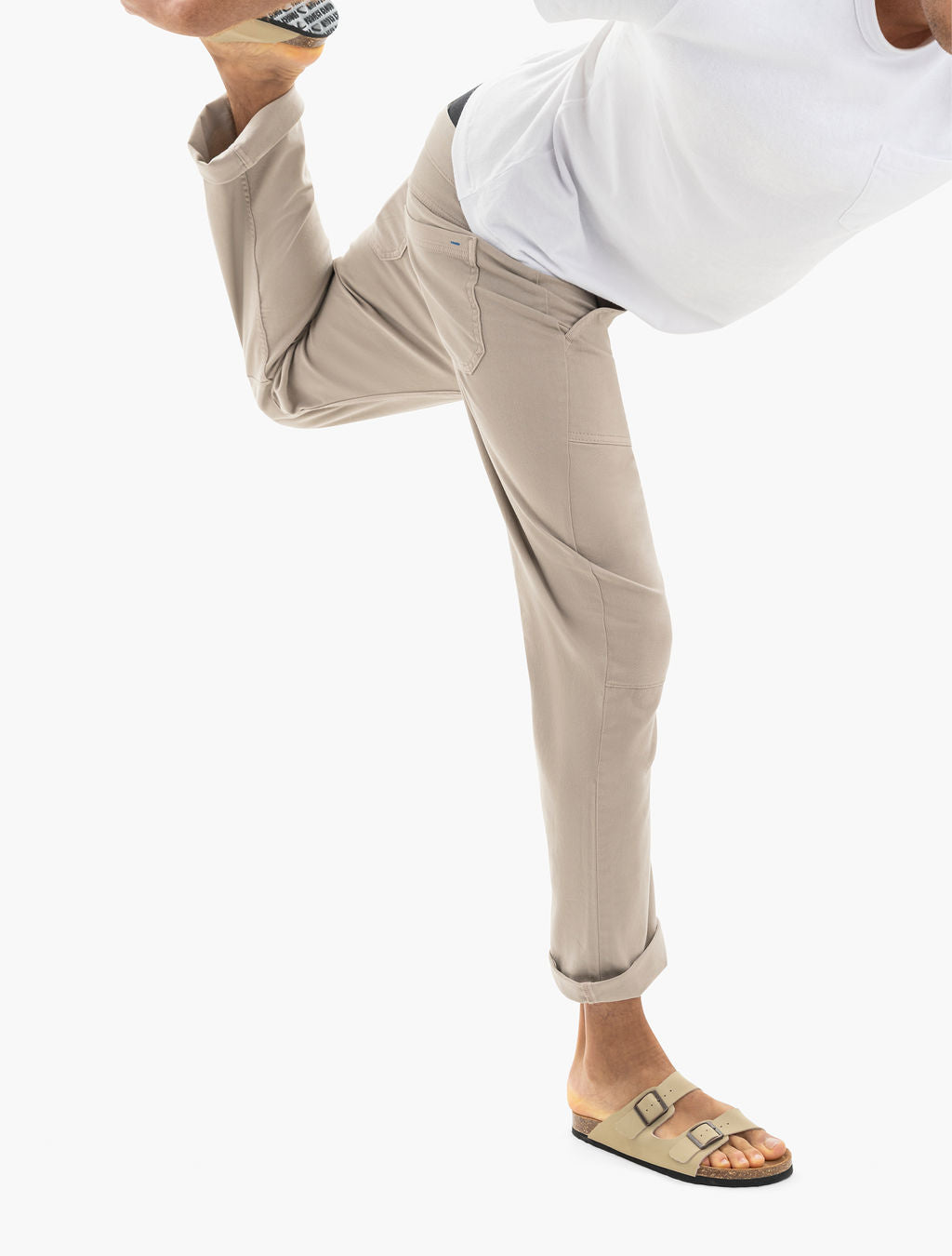 Person wearing rolled-cuff beige pants and white T-shirt balancing on one leg, showing beige two-strap sandals.