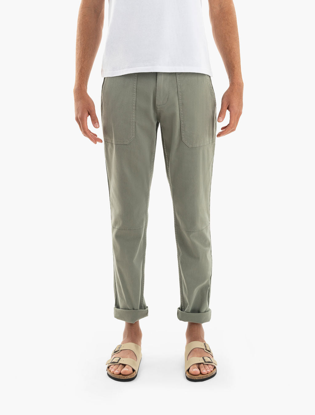 Olive-green tapered pants with front patch pockets and rolled cuffs, shown on a model wearing tan double-strap sandals.